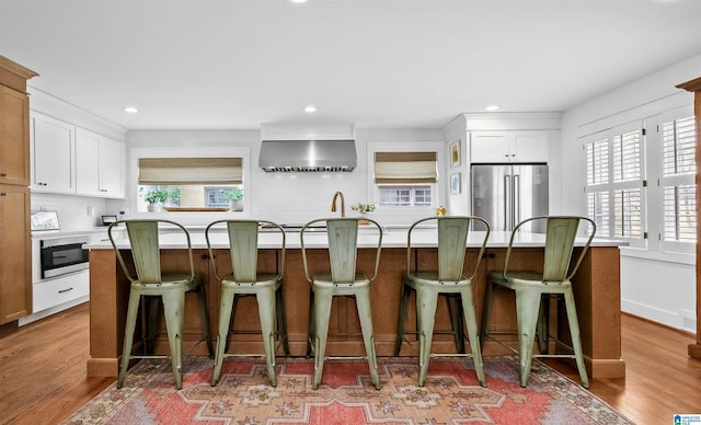 kitchen featuring wall chimney exhaust hood, high end fridge, light wood-style flooring, and white cabinets