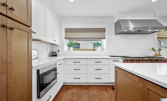 kitchen with dark wood finished floors, stainless steel microwave, light countertops, and wall chimney range hood