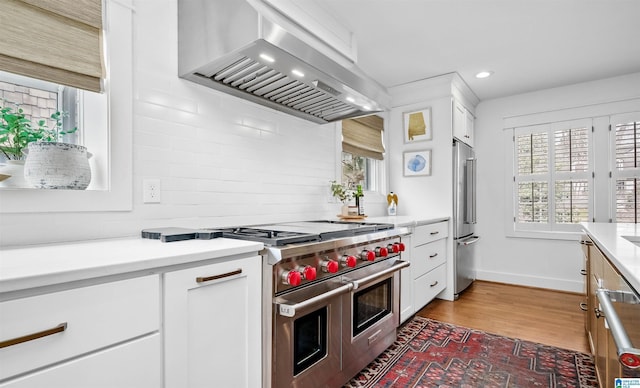 kitchen with high quality appliances, backsplash, wall chimney exhaust hood, white cabinets, and light countertops