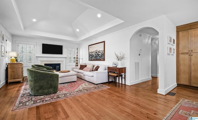 living room featuring visible vents, a tray ceiling, hardwood / wood-style flooring, arched walkways, and a glass covered fireplace