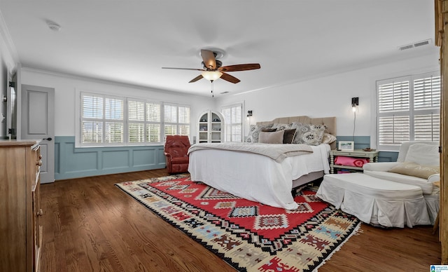 bedroom featuring visible vents, ceiling fan, ornamental molding, wood finished floors, and a decorative wall