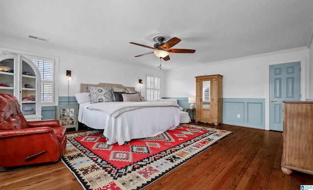 bedroom featuring wood finished floors, a wainscoted wall, visible vents, ceiling fan, and crown molding