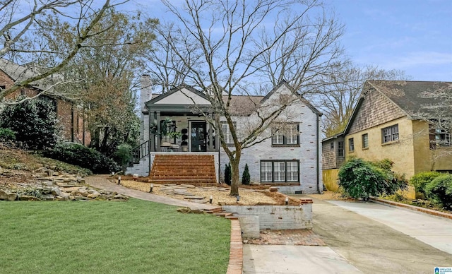 view of front of home featuring covered porch, driveway, a chimney, and a front yard