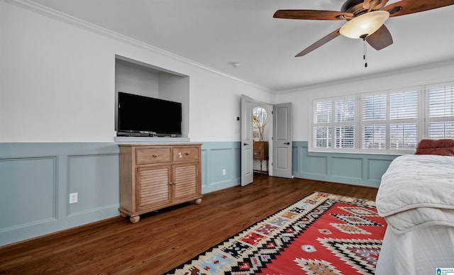 bedroom featuring a wainscoted wall, wood finished floors, crown molding, and a decorative wall