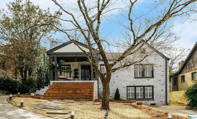 view of front facade featuring brick siding, a porch, and a chimney