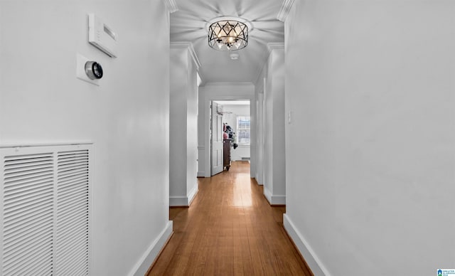 hall featuring baseboards, an inviting chandelier, wood finished floors, and crown molding