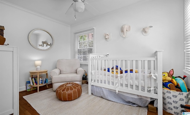 bedroom featuring crown molding, baseboards, a nursery area, wood finished floors, and a ceiling fan