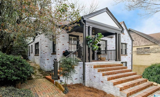 view of front facade with stairway, brick siding, and a porch