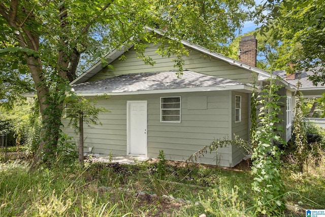 rear view of property featuring a shingled roof and a chimney