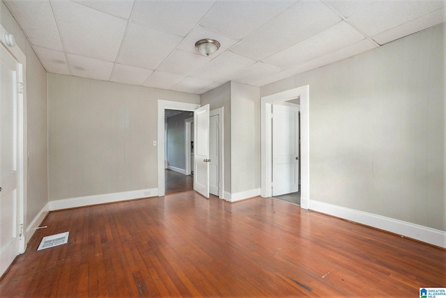 spare room with a paneled ceiling, wood-type flooring, visible vents, and baseboards