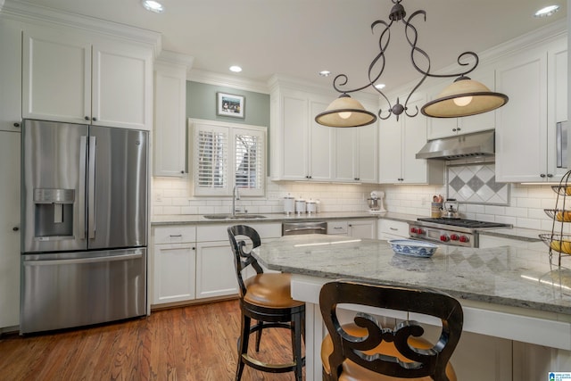 kitchen with under cabinet range hood, stainless steel appliances, a breakfast bar, a sink, and white cabinetry