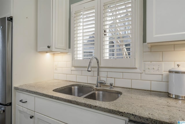 kitchen with light stone counters, a sink, white cabinets, freestanding refrigerator, and tasteful backsplash