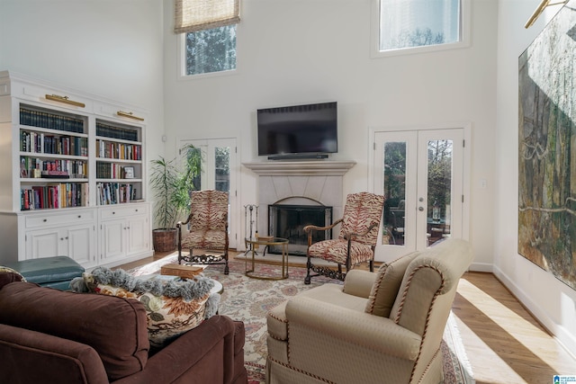 living room with french doors, a fireplace, a towering ceiling, wood finished floors, and baseboards