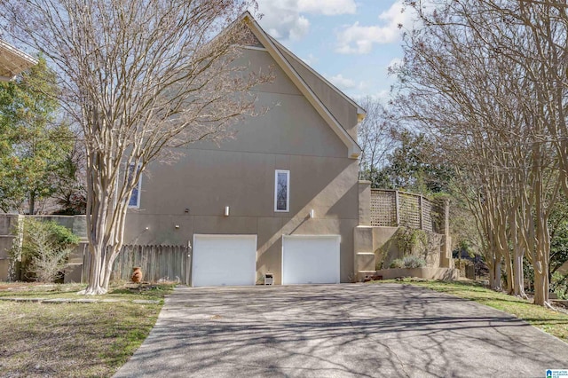 view of front of house featuring driveway, a garage, fence, and stucco siding