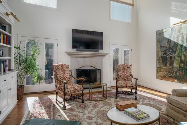 living area featuring a wealth of natural light, a tiled fireplace, a high ceiling, and wood finished floors