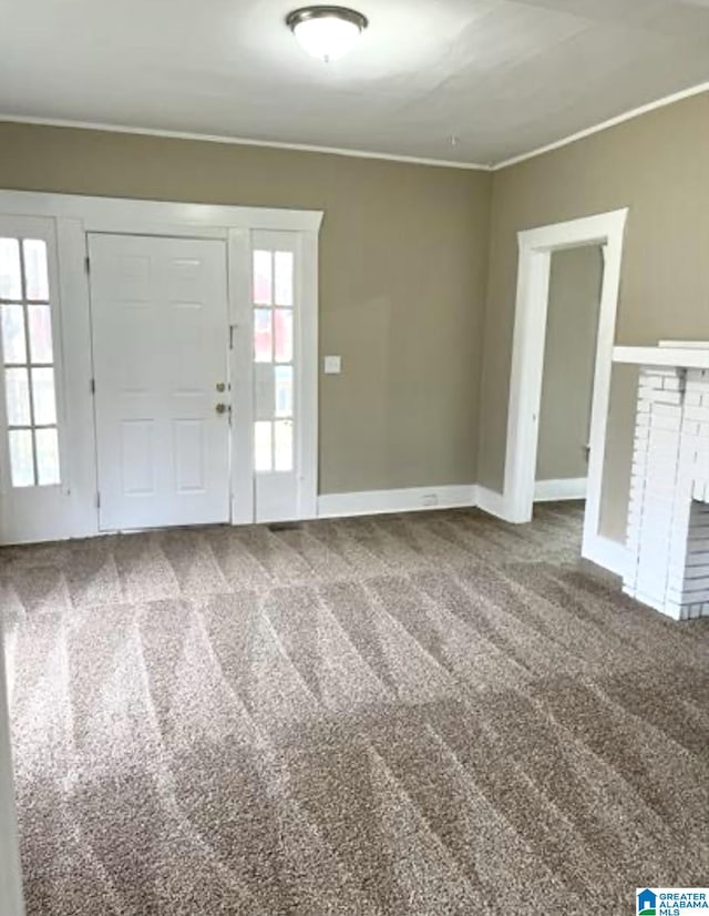 foyer entrance featuring baseboards, a brick fireplace, carpet flooring, and crown molding