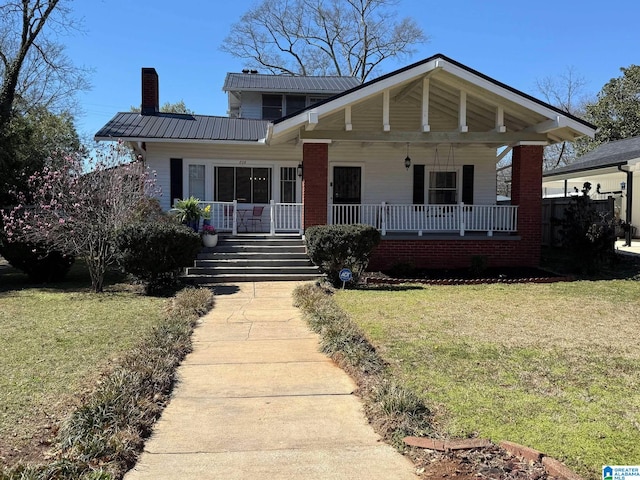 bungalow-style home featuring covered porch, metal roof, a front lawn, and a chimney