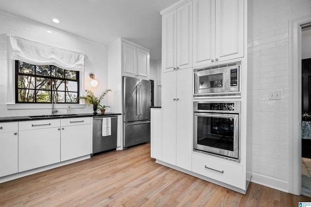 kitchen featuring stainless steel appliances, dark countertops, light wood-style flooring, white cabinets, and a sink