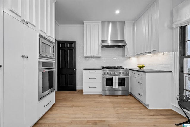 kitchen featuring wall chimney range hood, dark countertops, appliances with stainless steel finishes, and white cabinets