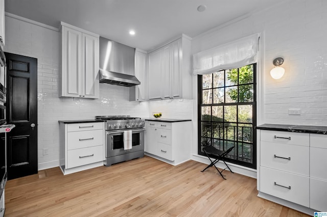 kitchen with decorative backsplash, dark countertops, wall chimney exhaust hood, high end stainless steel range oven, and light wood-type flooring