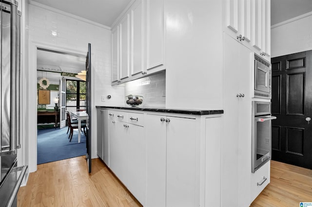 kitchen with light wood finished floors, dark countertops, stainless steel appliances, white cabinetry, and backsplash