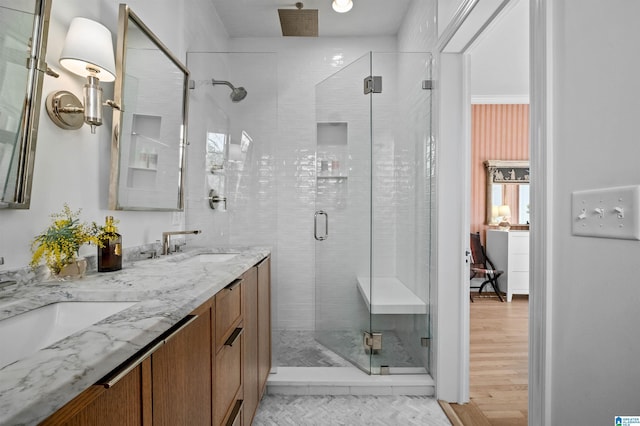 bathroom featuring double vanity, a shower stall, a sink, and wood finished floors