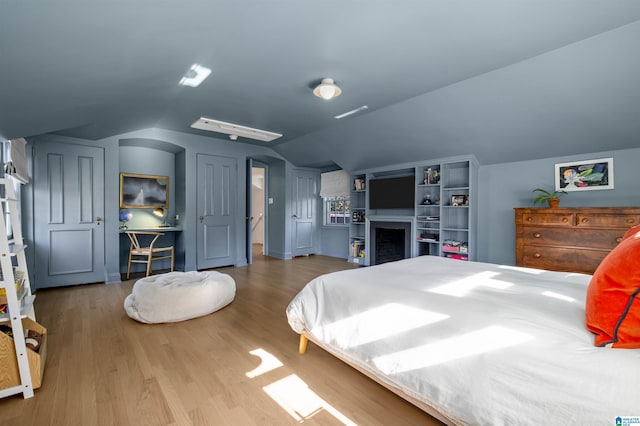 bedroom featuring a fireplace, vaulted ceiling, and wood finished floors