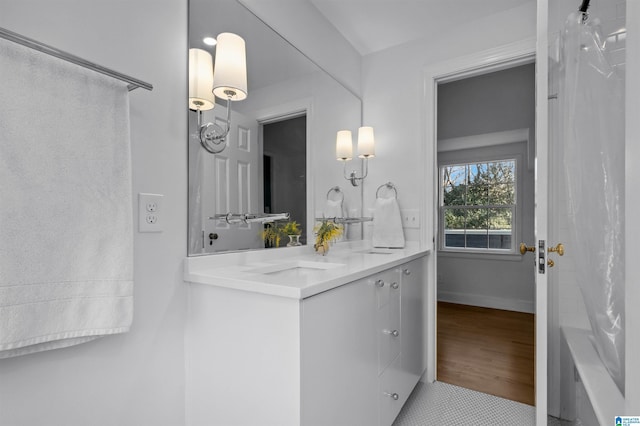 bathroom with double vanity, baseboards, a sink, and wood finished floors