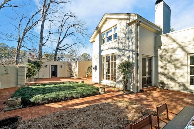 back of house featuring a chimney, fence, and stucco siding