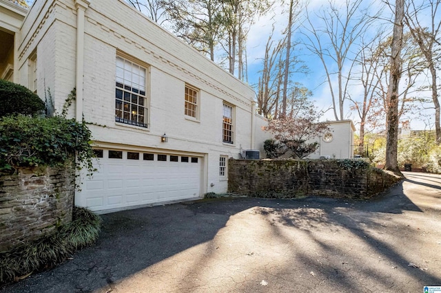 view of home's exterior with brick siding, driveway, an attached garage, and central AC unit