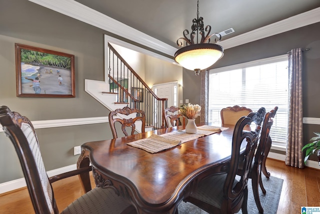 dining space with baseboards, wood-type flooring, visible vents, and crown molding