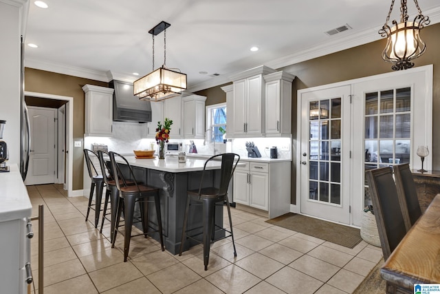 kitchen featuring a breakfast bar area, light countertops, visible vents, light tile patterned flooring, and wall chimney exhaust hood