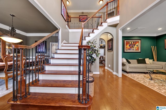 stairs featuring baseboards, arched walkways, wood finished floors, a high ceiling, and crown molding