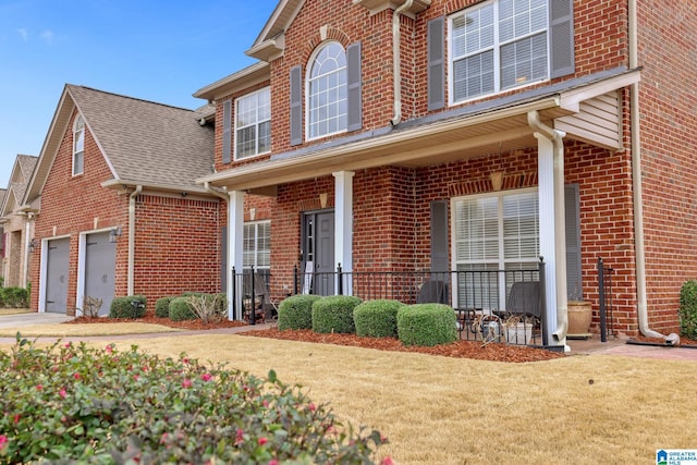 traditional-style home featuring a garage, driveway, a porch, a front lawn, and brick siding