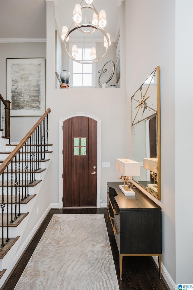 entrance foyer with ornamental molding, a notable chandelier, baseboards, and wood finished floors