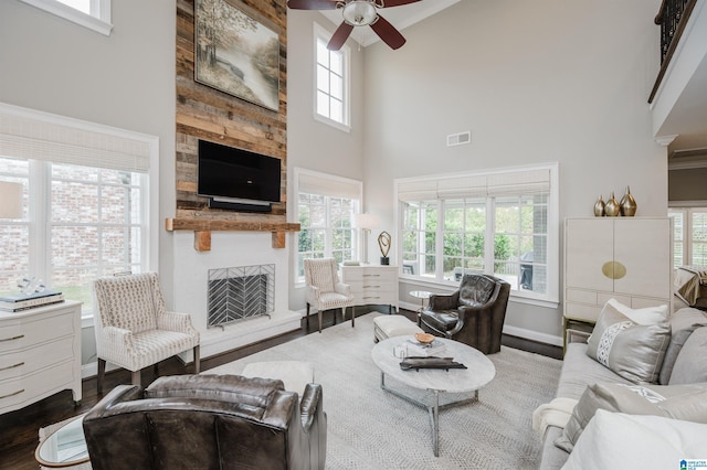 living area with a large fireplace, baseboards, visible vents, a towering ceiling, and wood finished floors