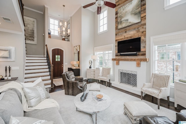 living area featuring a large fireplace, visible vents, stairway, wood finished floors, and crown molding