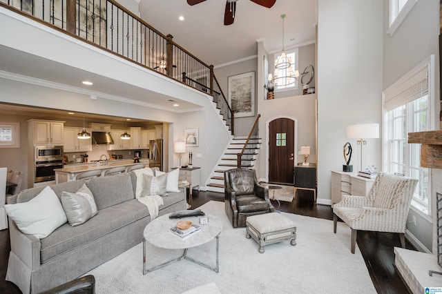 living room featuring crown molding, a towering ceiling, stairway, wood finished floors, and baseboards