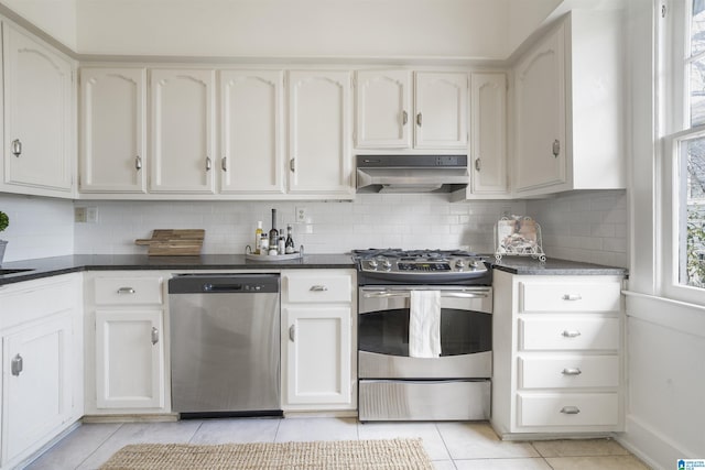 kitchen featuring stainless steel appliances, dark countertops, decorative backsplash, white cabinetry, and under cabinet range hood