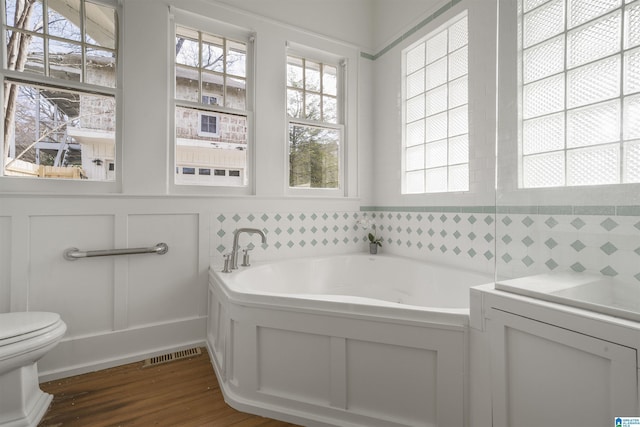 bathroom featuring visible vents, plenty of natural light, toilet, and a bath