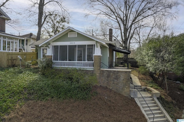 back of house featuring a sunroom, a chimney, fence, and brick siding