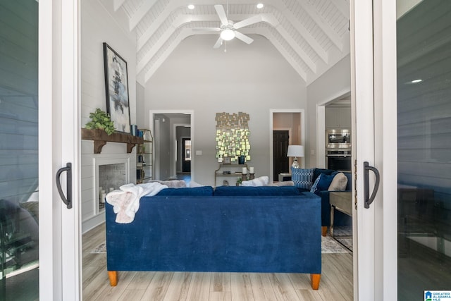 living room featuring high vaulted ceiling, a large fireplace, wood finished floors, a ceiling fan, and beamed ceiling