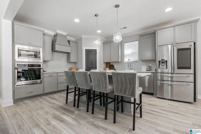 kitchen with a center island, gray cabinets, light countertops, appliances with stainless steel finishes, and premium range hood