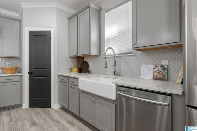 kitchen featuring light wood finished floors, gray cabinets, appliances with stainless steel finishes, ornamental molding, and a sink