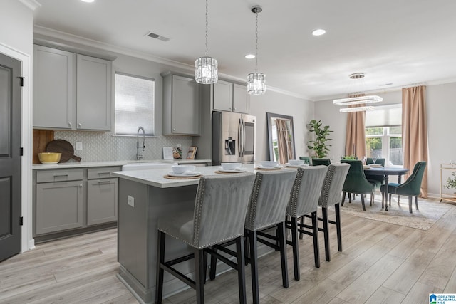 kitchen featuring visible vents, crown molding, gray cabinetry, a kitchen bar, and stainless steel refrigerator with ice dispenser