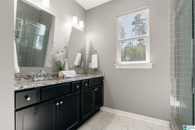 bathroom with marble finish floor, tiled shower, a sink, and baseboards