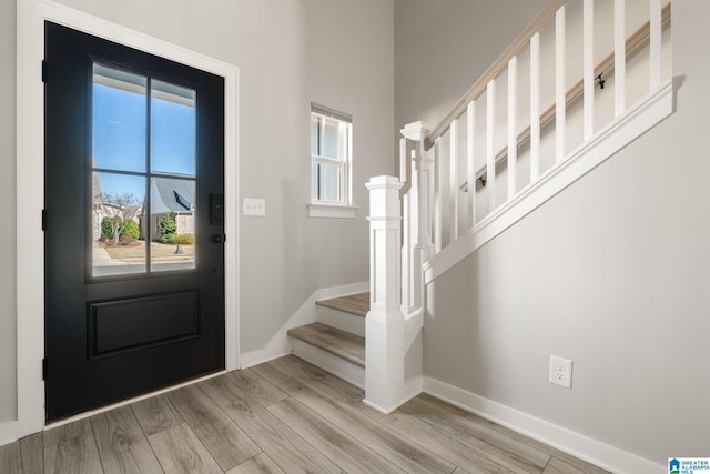 entryway with light wood-type flooring, baseboards, and stairs