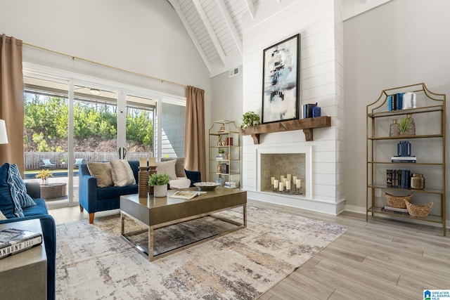 living room featuring high vaulted ceiling, a fireplace, wood finished floors, and visible vents