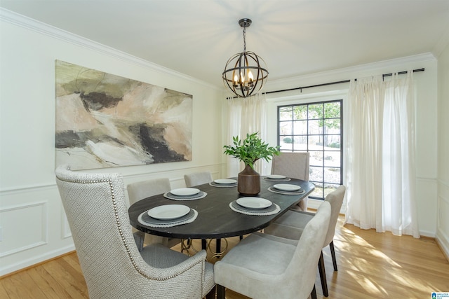 dining room with a decorative wall, ornamental molding, light wood-type flooring, and a chandelier