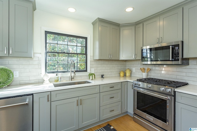 kitchen featuring gray cabinetry, a sink, appliances with stainless steel finishes, light wood finished floors, and light countertops